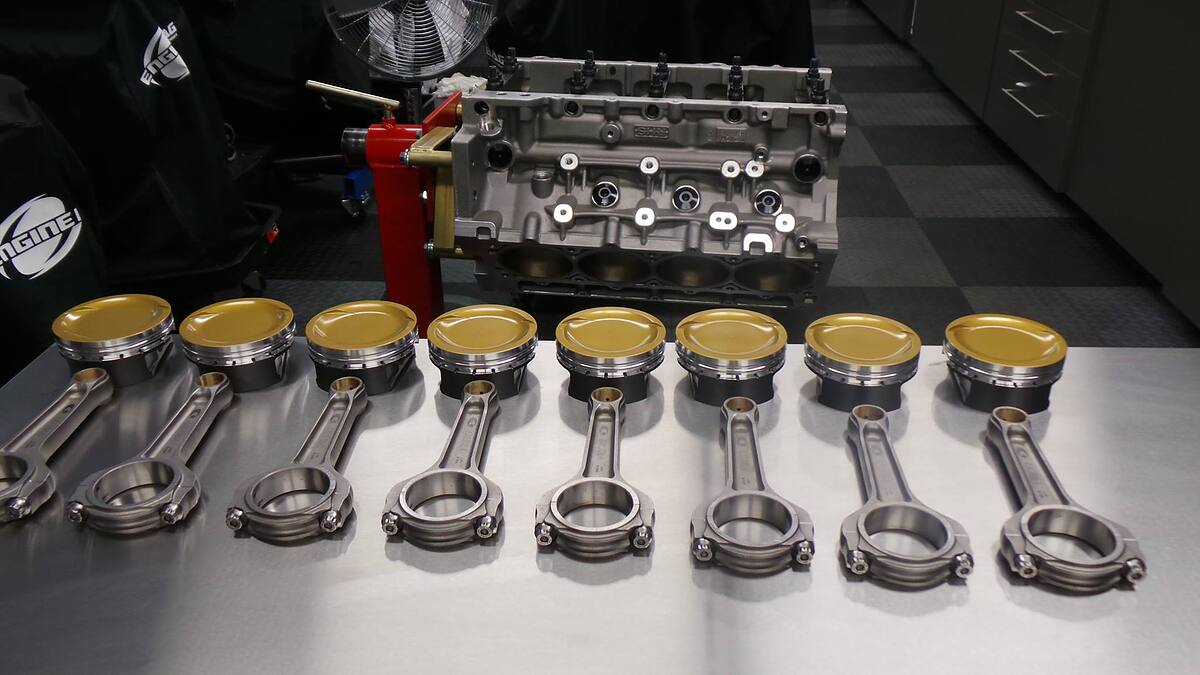 Eight forged connecting rods and gold-coated pistons laid out in front of a bare LS engine block at Sam's Performance